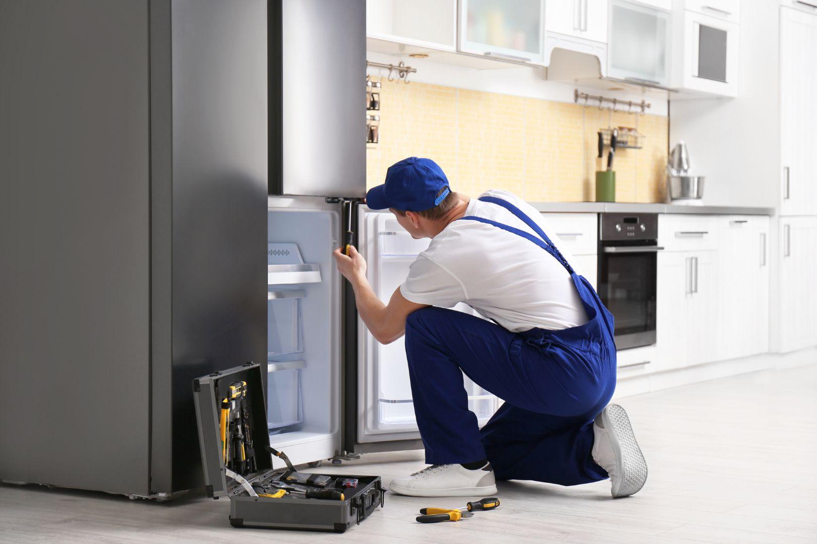 Técnico da Ômega Refrigeração ajoelhado realizando conserto de geladeira na cozinha do cliente